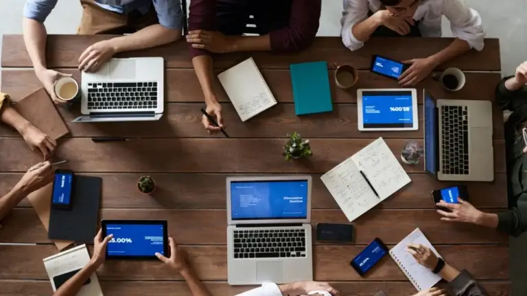 a bunch of technology gathered at a table where a lot of people are sat around discussing the statistics