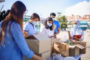 a group of people packing up boxes outside on a sunny day wearing masks