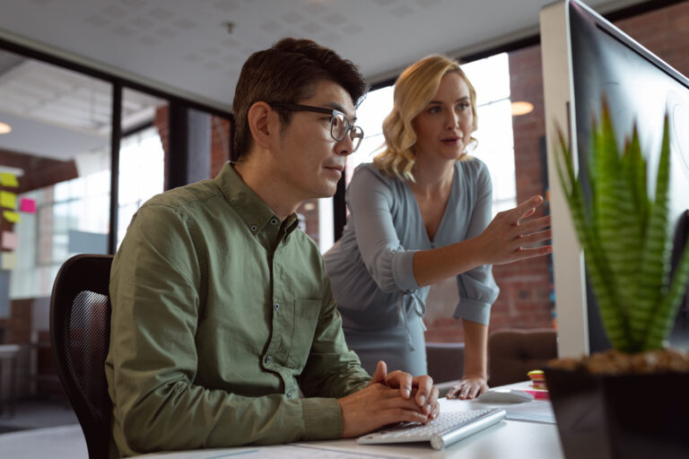 Diverse male and female colleague looking at computer screen and discussing at desk in office