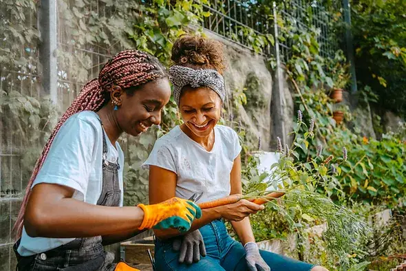 two women laughing while gardening holding carrots