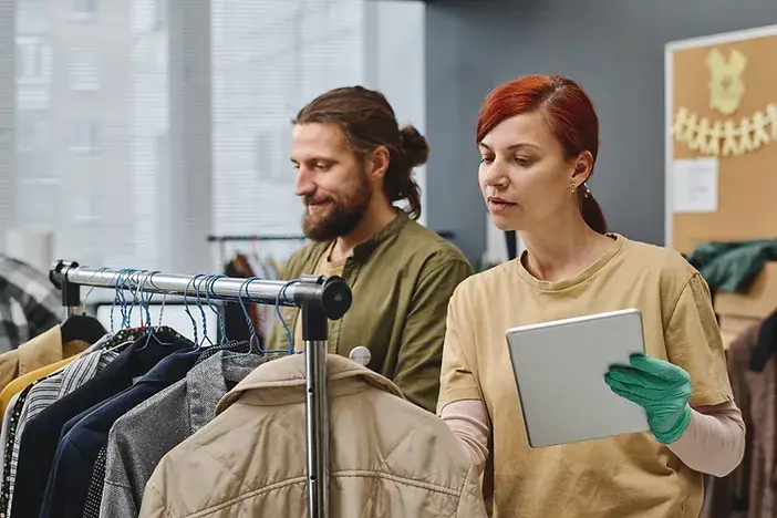 a man and woman browsing through a rack of clothes