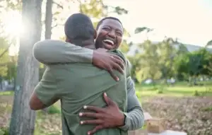 Image of two men hugging outside in a park, the men are joyful to see each other