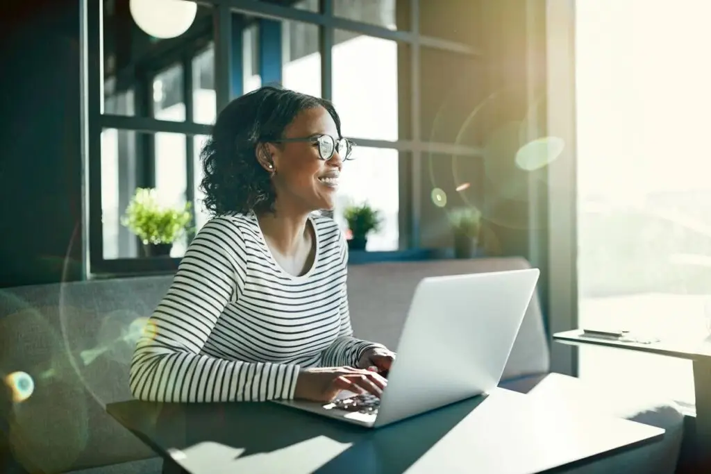 Image of a woman sitting at a table on her computer staring at the window smiling