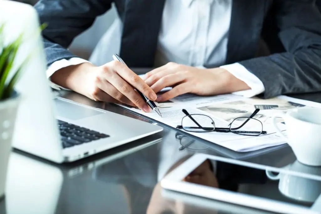 Image of a businessman's desk, including a computer, tablet, glasses, and papers