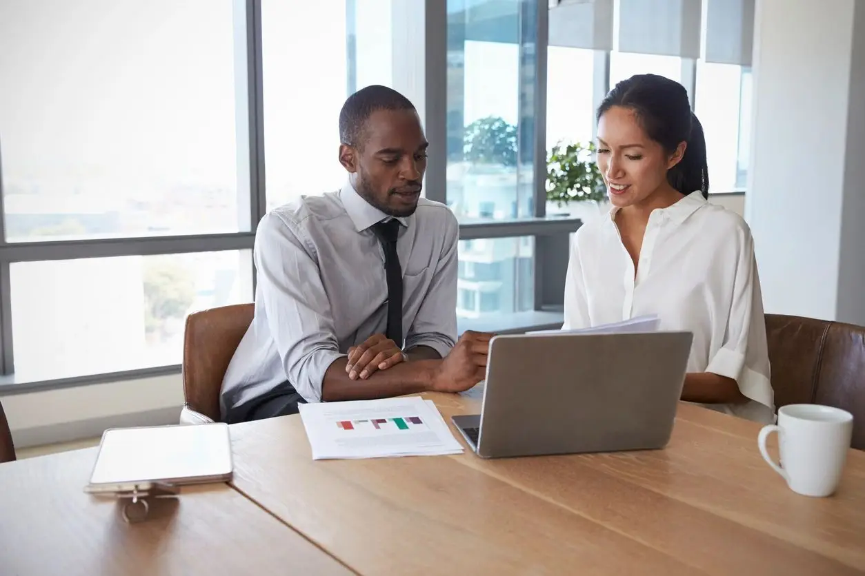 Two people having a conversation while both looking at a laptop on the table