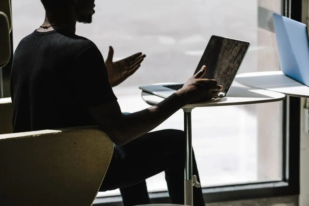 Image of a man sitting in a chair looking at the computer gesturing with his hands