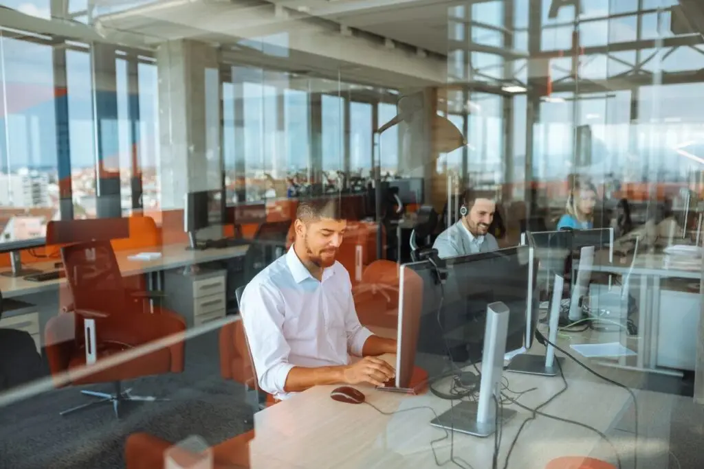 Image of an office from outside a window with people working at their computers