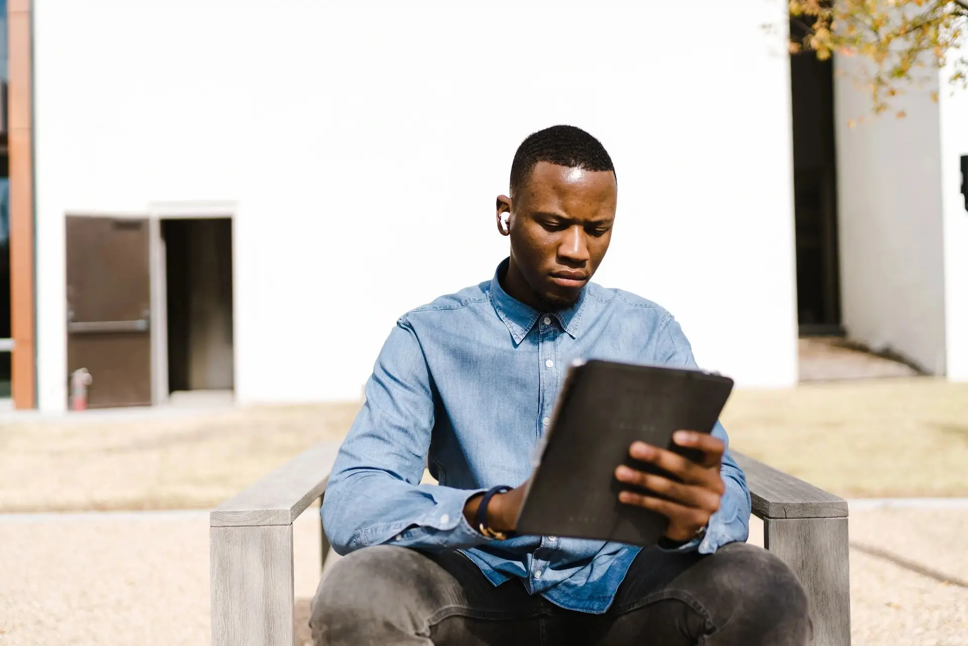 Man sitting on a chair outside with headphones in, looking down at an ipad