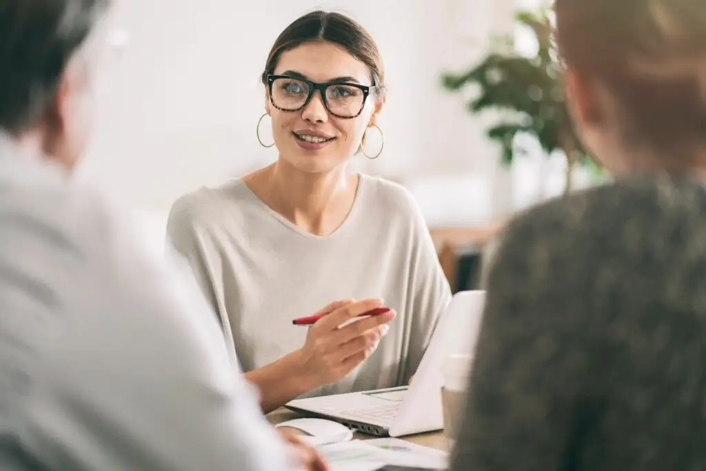 Image of a woman with glasses over her laptop discussing with two other people