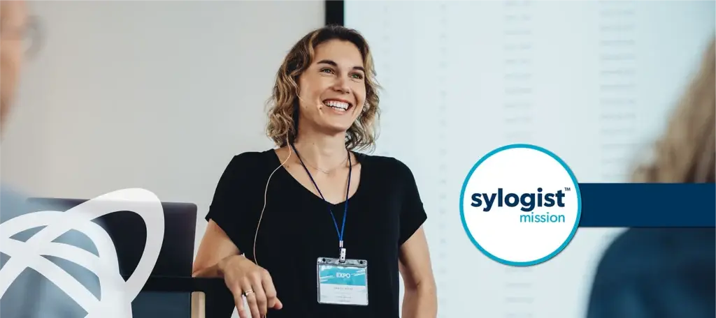 Image of a woman standing in front of a room with a microphone on smiling