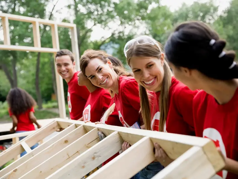 Image of a group of volunteers in red shirts help assemble wood objects happily