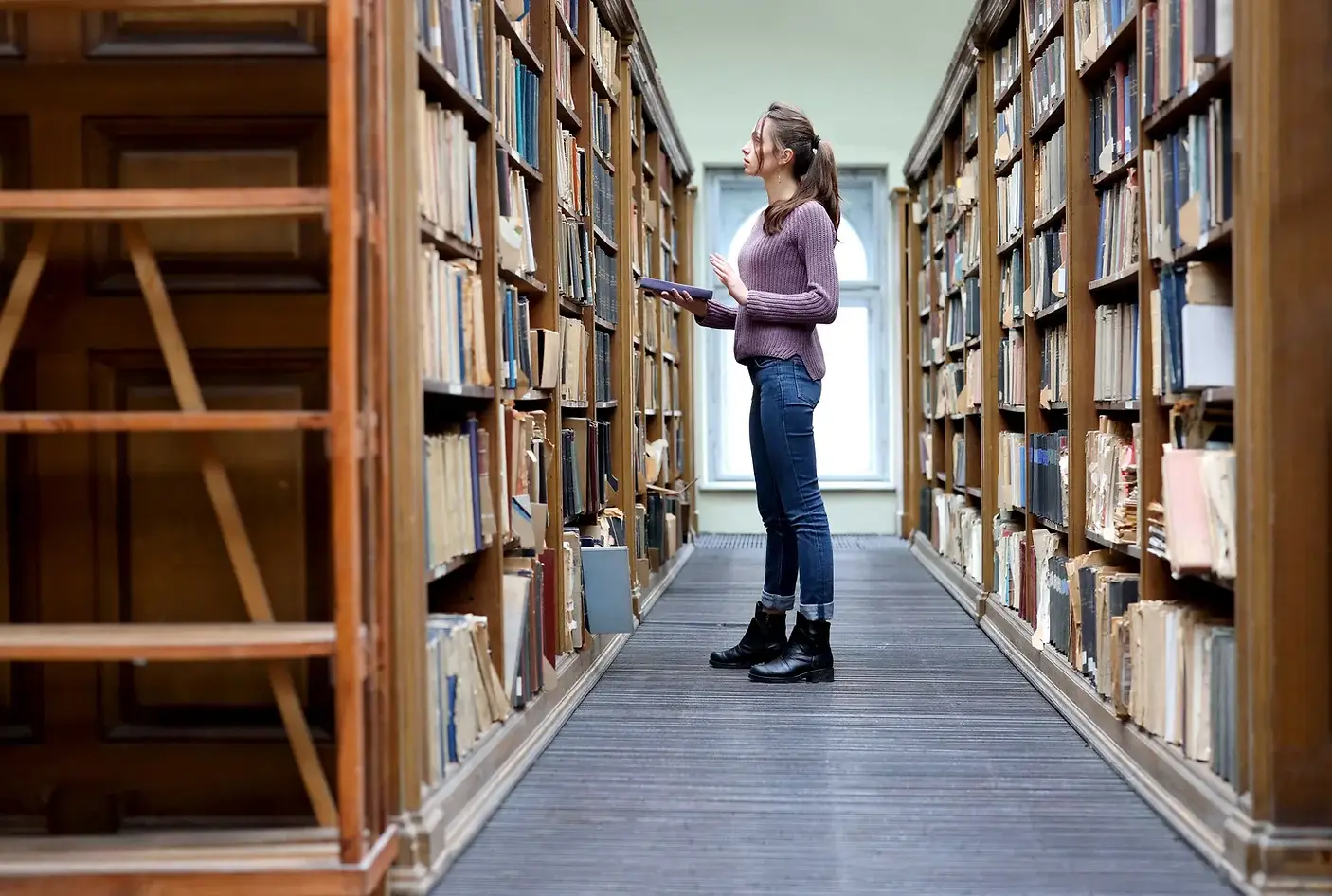 Image of a woman browsing in a library from down the row