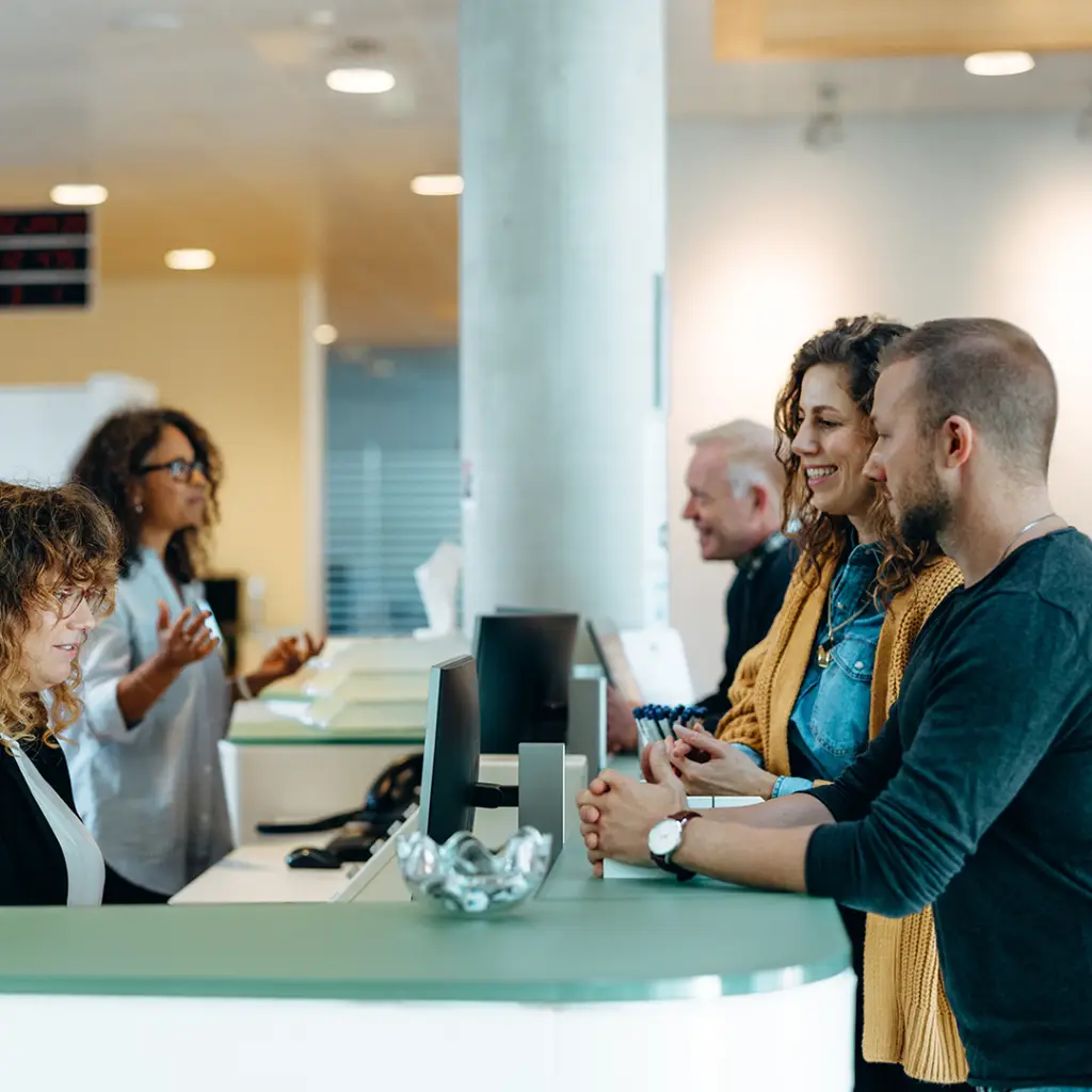 People standing at counter talking to woman