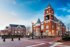 Historic red brick clock tower building with a decorative clock, flanked by modern structures, set against a vibrant blue sky